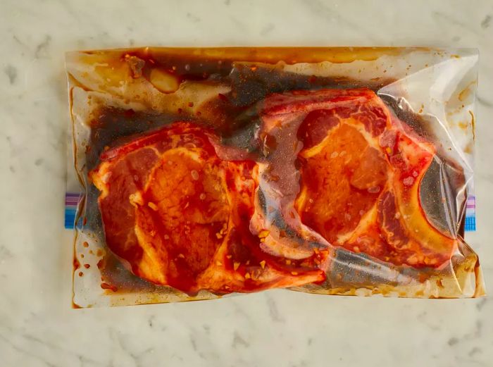 Pork chops marinating in sauce inside a plastic bag.