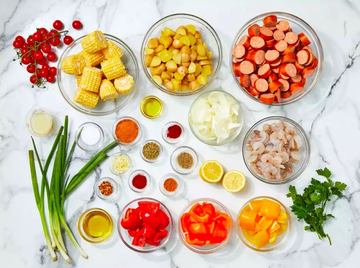 All the ingredients for the sheet pan shrimp and sausage bake are neatly arranged on a marble countertop.