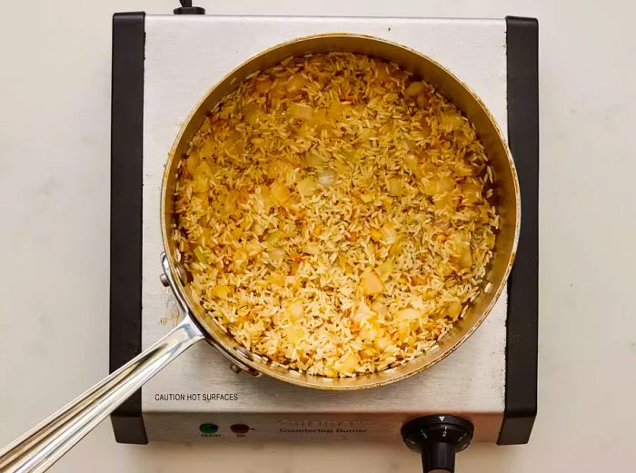 A pan filled with rice, sautéed onions, and garlic