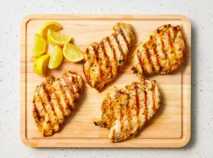 Grilled juicy chicken breasts with lemon wedges on a rustic wooden cutting board