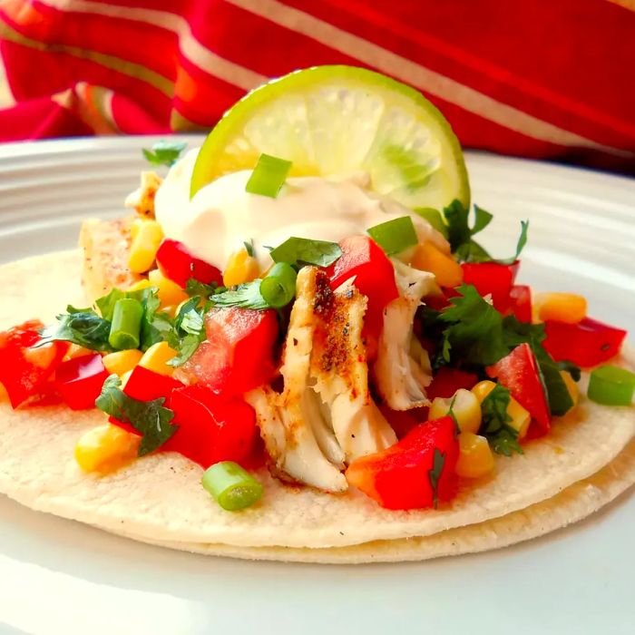 A close-up shot of a Fiery Fish Taco with Crunchy Corn Salsa, garnished with a lime wedge on a plate.