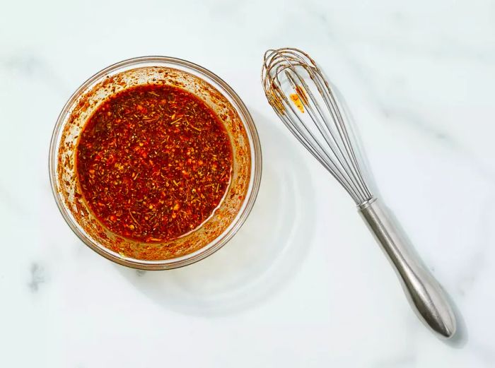 A small bowl filled with a well-mixed blend of olive oil, Creole seasoning, lemon juice, garlic, Italian seasoning, paprika, red pepper flakes, salt, and pepper.