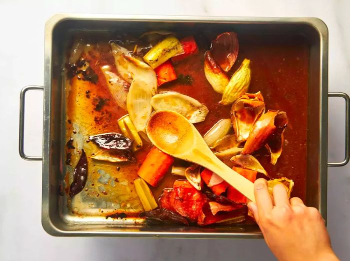 A person deglazing the roasting pan to make au jus sauce.