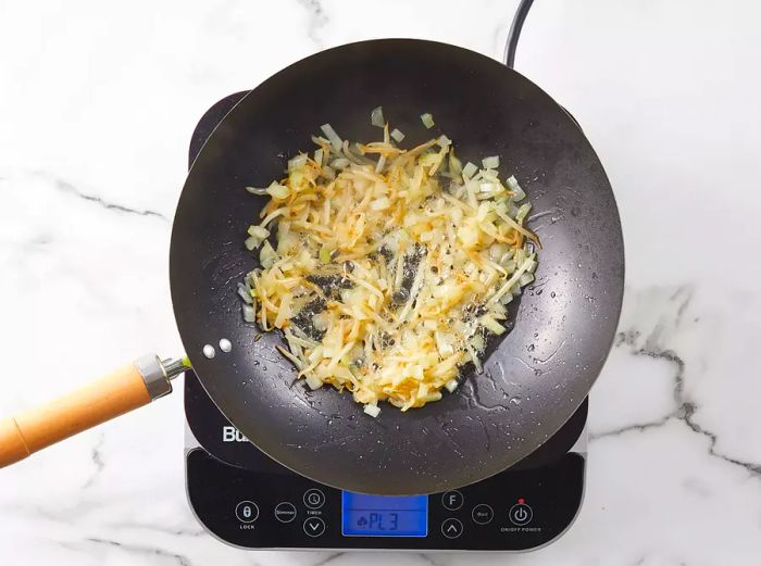 Bean sprouts and onions cooking and browning in a wok with vegetable oil.