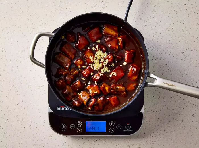 A pan of sweet and sour pork with minced garlic.