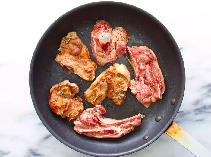 Overhead shot of lamb shoulder searing in a skillet