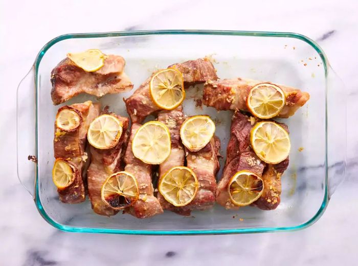 A baking dish with succulent roasted ribs topped with fresh lemon slices and garlic