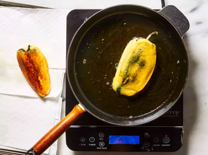 Chiles fried to a golden brown, resting on paper towels to drain excess oil