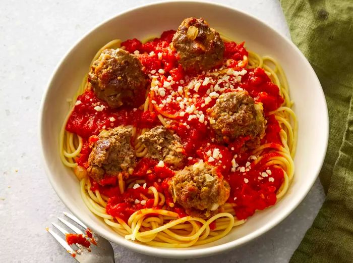 A plate of spaghetti topped with tomato sauce, meatballs, and a sprinkle of parmesan cheese