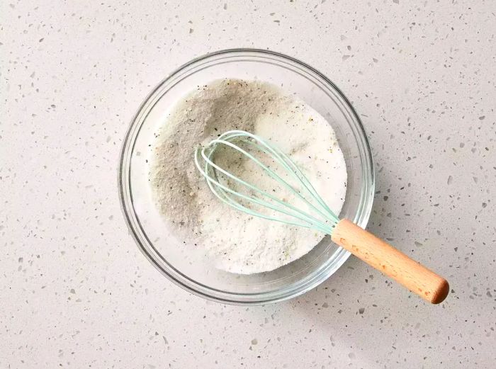 A bowl containing sugar, flour, salt, pepper, and mustard being mixed together.