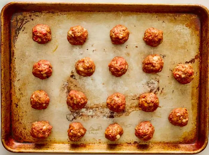 A baking sheet lined with uncooked meatballs