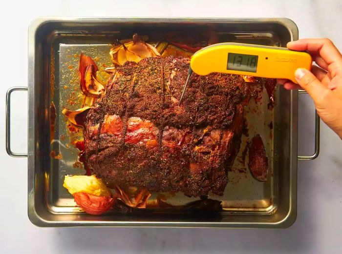 A person checking the internal temperature of a cooked prime rib with a thermometer.