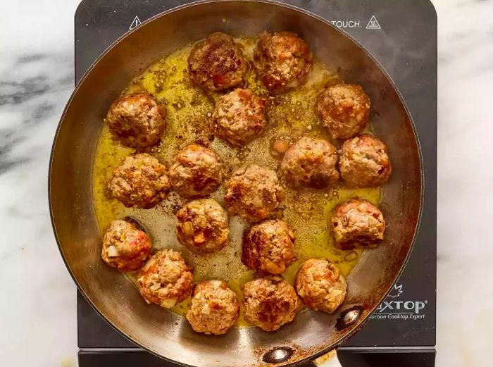 A skillet with meatballs cooking in a mixture of melted butter and olive oil