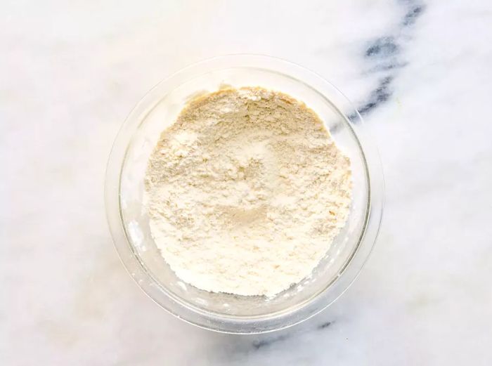 A small glass bowl containing flour, nutmeg, salt, and white pepper