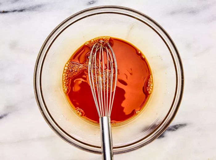 A small bowl containing a mixture of soy sauce, vinegar, and cornstarch, with a whisk for stirring.