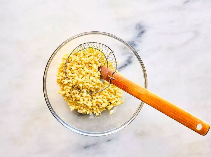 A bowl filled with cooked spaetzle, accompanied by a spider skimmer