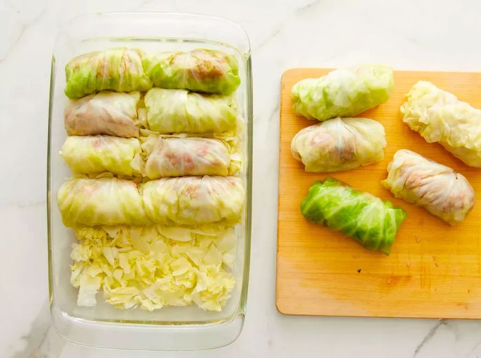 A top-down view of a baking dish as stuffed cabbage rolls are placed on a bed of chopped cabbage.