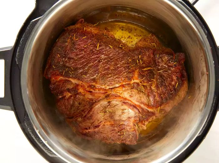 A top-down view of a roast cooking inside a pressure cooker.