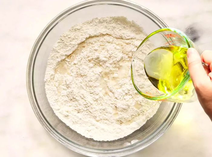 A bird's-eye view of flour in a bowl with oil in a measuring cup.