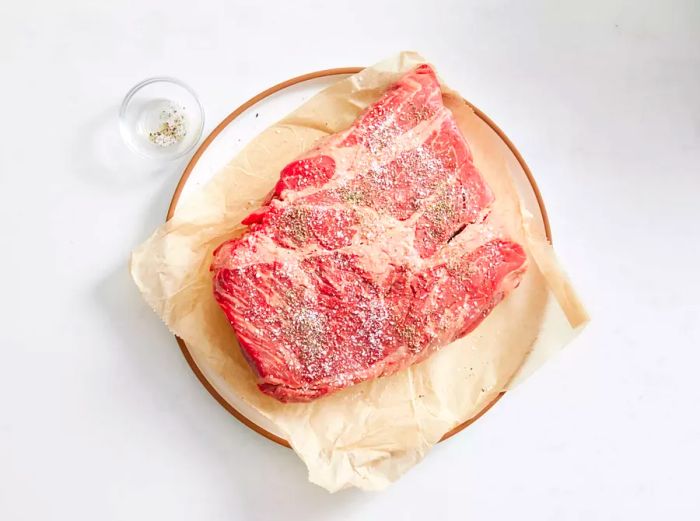 Place the chuck roast on parchment paper, seasoned with salt and black pepper.