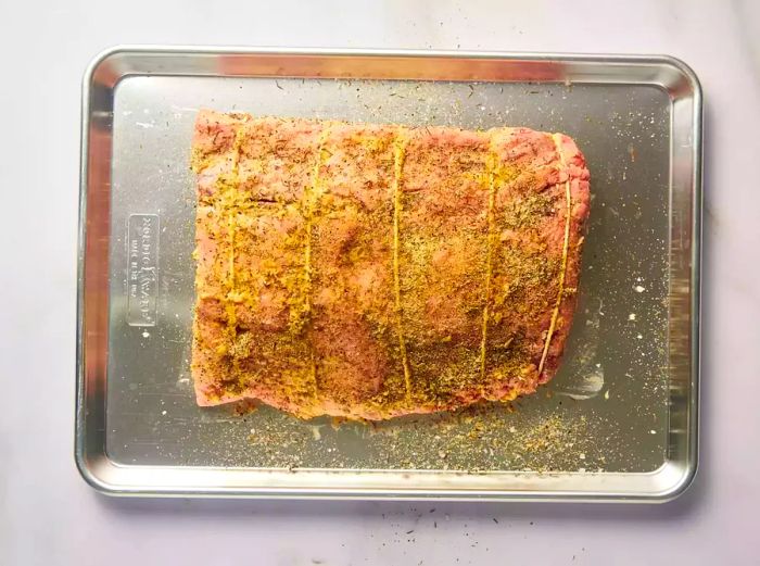 Prime rib, tied and seasoned with horseradish and mustard, resting in a baking dish.