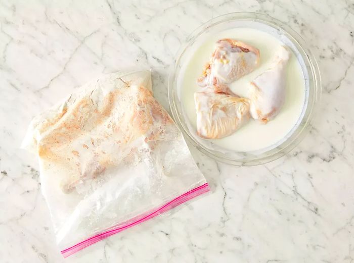 An overhead shot of chicken being dipped into a buttermilk mixture and placed into a resealable plastic bag with the flour mixture.