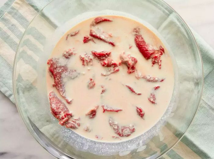 An overhead view of venison slices soaking in a mixture of milk and hot sauce