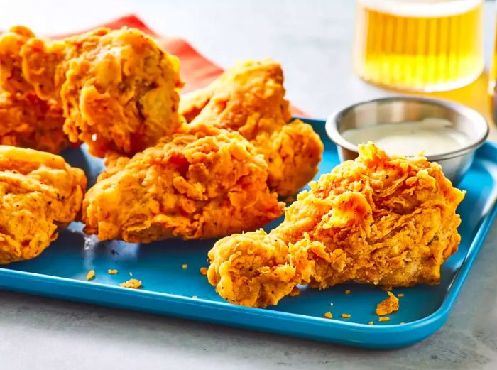 A blue tray filled with crispy fried chicken and a small cup of dipping sauce