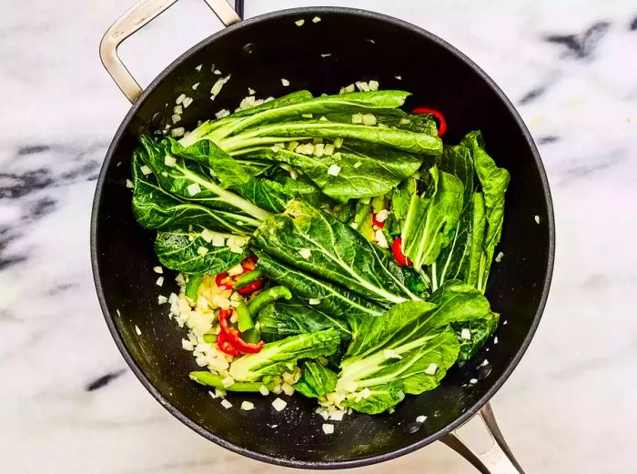 A wok filled with bok choy stalks, red chiles, onion, and bell pepper being stir-fried