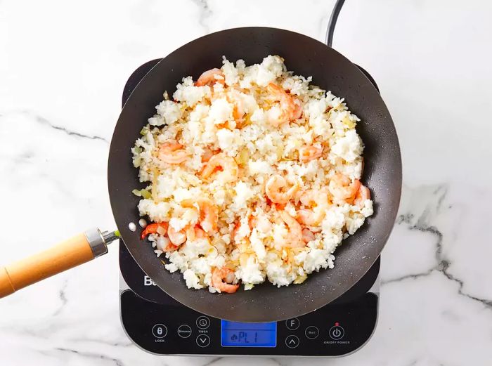 Rice and shrimp are added to the wok with onions and bean sprouts, ready to cook together.