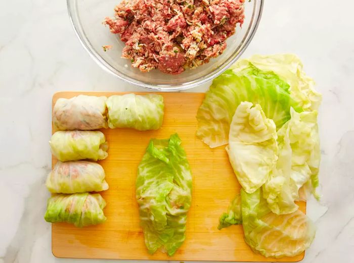 An overhead shot of a cutting board with cabbage leaves being filled with the prepared mixture.