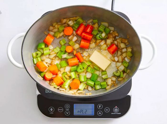 A large pot containing chopped carrots, onions, celery, and butter