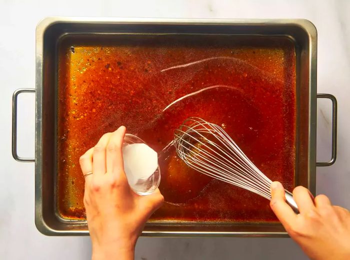 A person adding a cornstarch slurry to the beef broth to thicken the sauce.