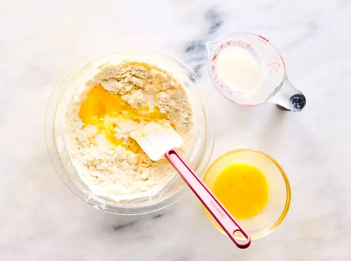 A glass bowl with a seasoned flour mixture, while eggs and milk are being incorporated