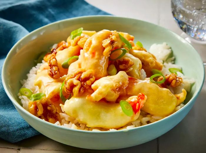 A serving of honey walnut shrimp over white rice, garnished with sliced green onions