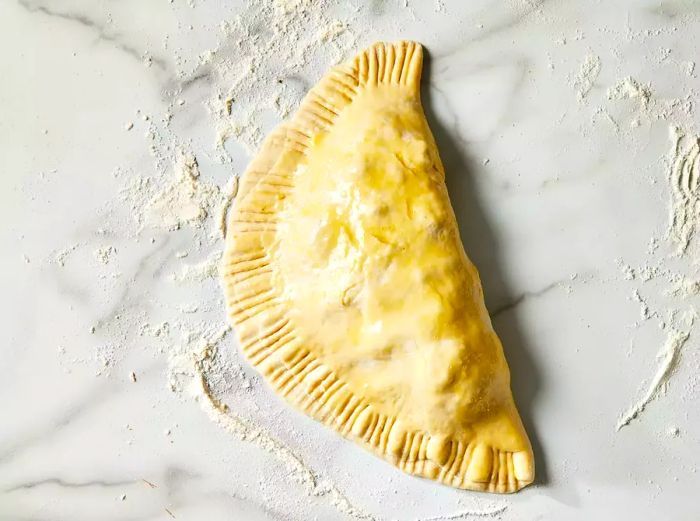 A top-down view of an unbaked calzone brushed with egg wash