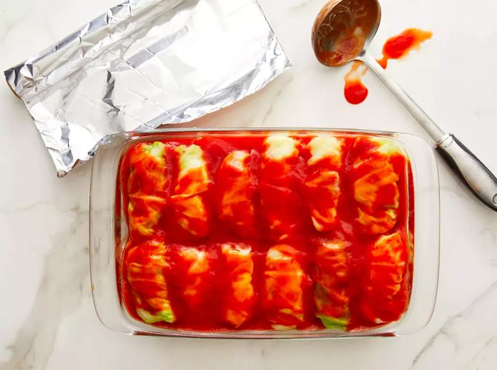 An overhead view of a baking dish filled with stuffed cabbage rolls, covered in tomato sauce, ready for the oven.