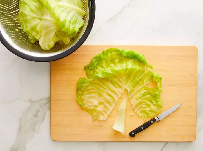 A top-down view of cabbage on a cutting board with the rib being carefully sliced out