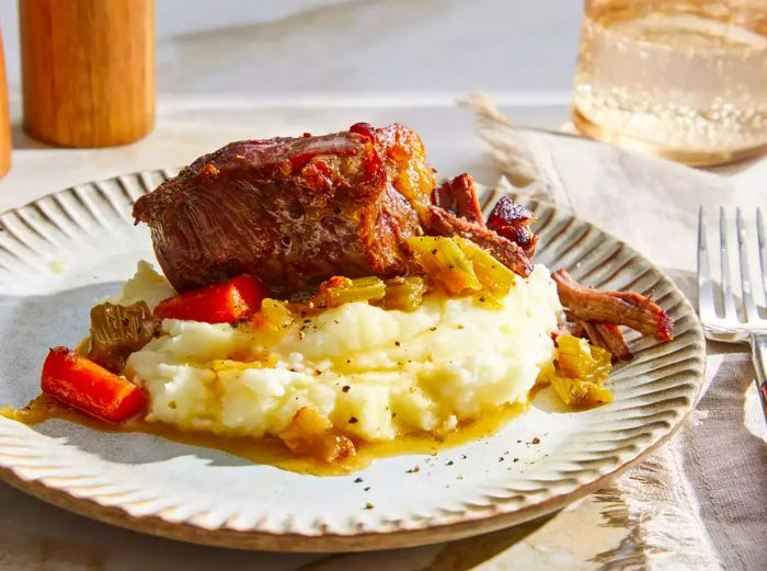 A plate of hearty beef pot roast with carrots and celery served over creamy mashed potatoes