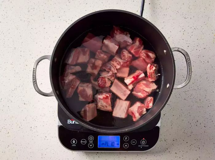 A large pot filled with pork spareribs submerged in water.