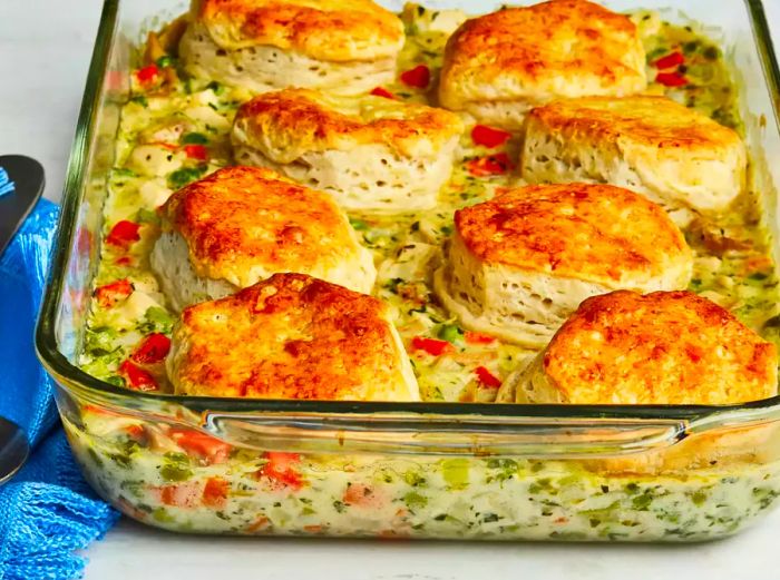 A low-angle view of a chicken pot pie with a biscuit crust served in a casserole dish.