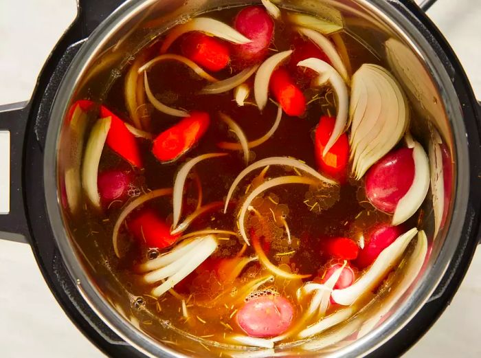 A top-down view of a pressure cooker with broth, oil, and vegetables simmering inside.