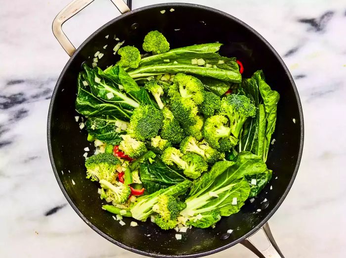 A wok filled with a colorful mix of broccoli, bok choy, onions, red chiles, and bell pepper