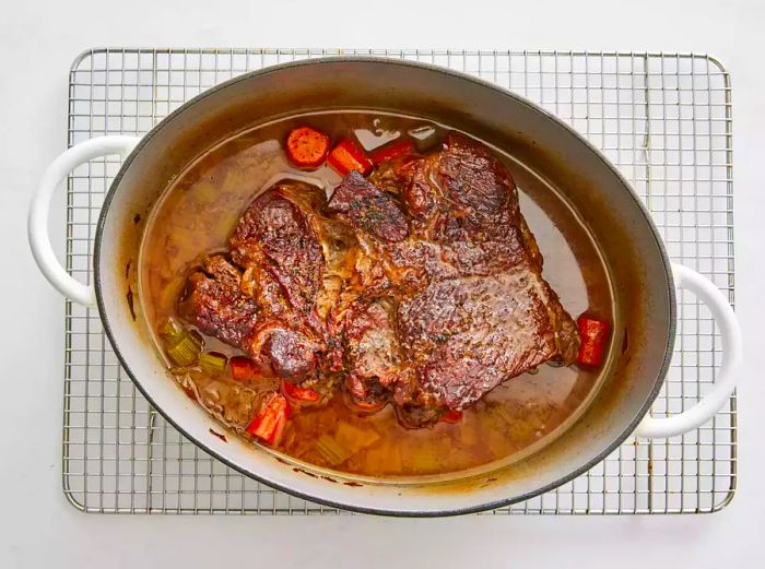 A large pot of beef pot roast resting on a white cooling rack