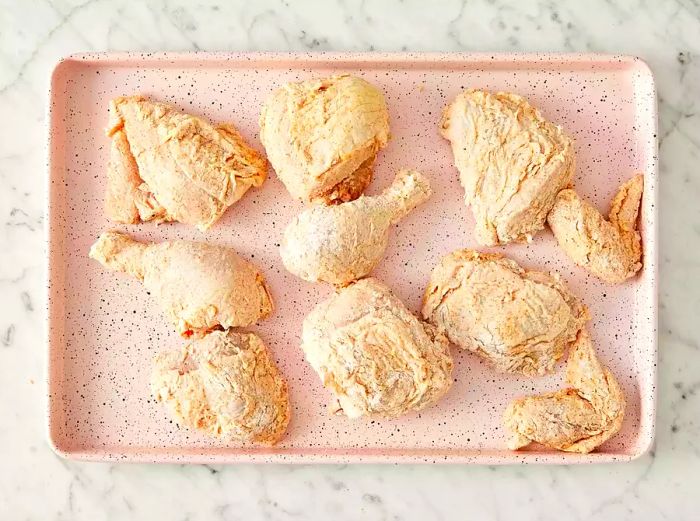 An overhead view of the floured, covered chicken pieces resting on a baking dish.