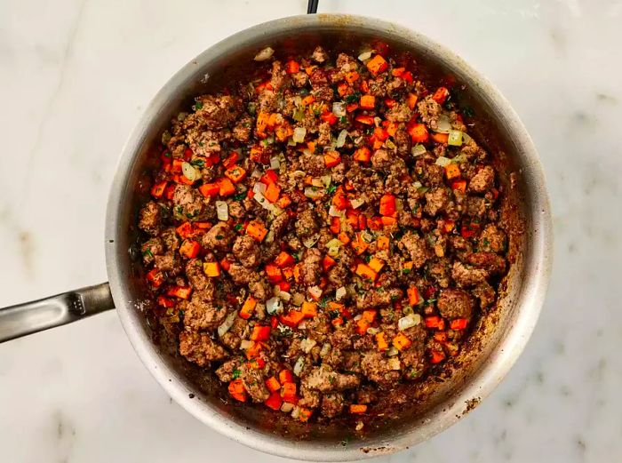 Ground beef with carrots and onions cooking in a skillet.