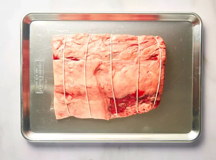 Prime rib, tied and placed on a baking sheet, ready for cooking.