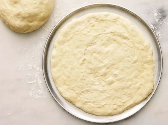 A top-down view of pizza dough being stretched on a pizza pan.