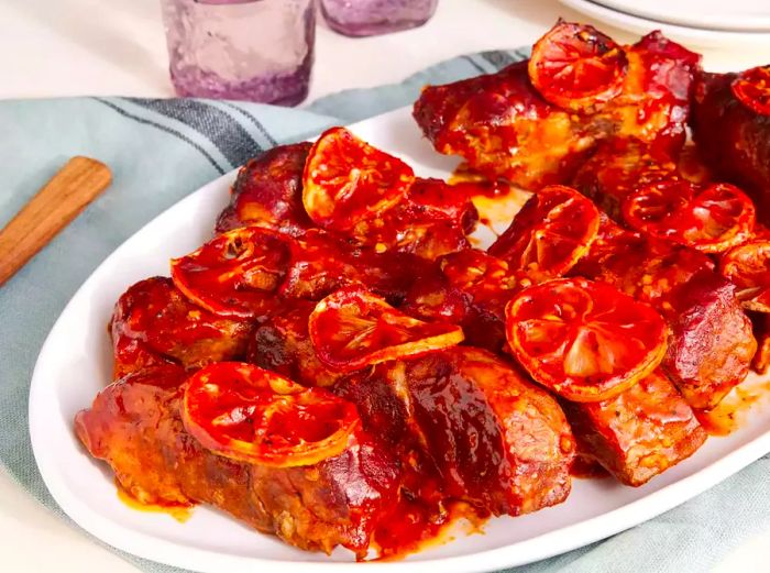 A platter of BBQ country-style ribs drenched in barbecue sauce and garnished with roasted lemon slices