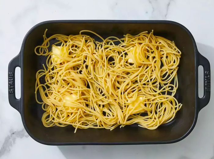 Butter slices placed at the bottom of the dish with spaghetti noodles layered on top